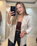 Blazer bege claro, vista frontal no espelho; lapela clássica, mangas dobradas, fechamento por botão e comprimento ao quadril.