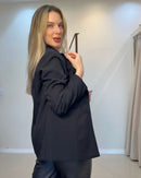 Blazer preto, vista lateral mostrando costas; mangas longas com botões no punho, costuras estruturadas e corte reto.