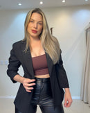 Blazer preto, meia-frente aberta; lapela tradicional, mangas levemente dobradas e caimento alongado que veste o quadril.